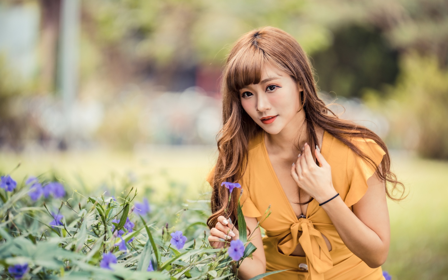 Красивая девушка азиатка в желтом платье у фиолетовых цветов 