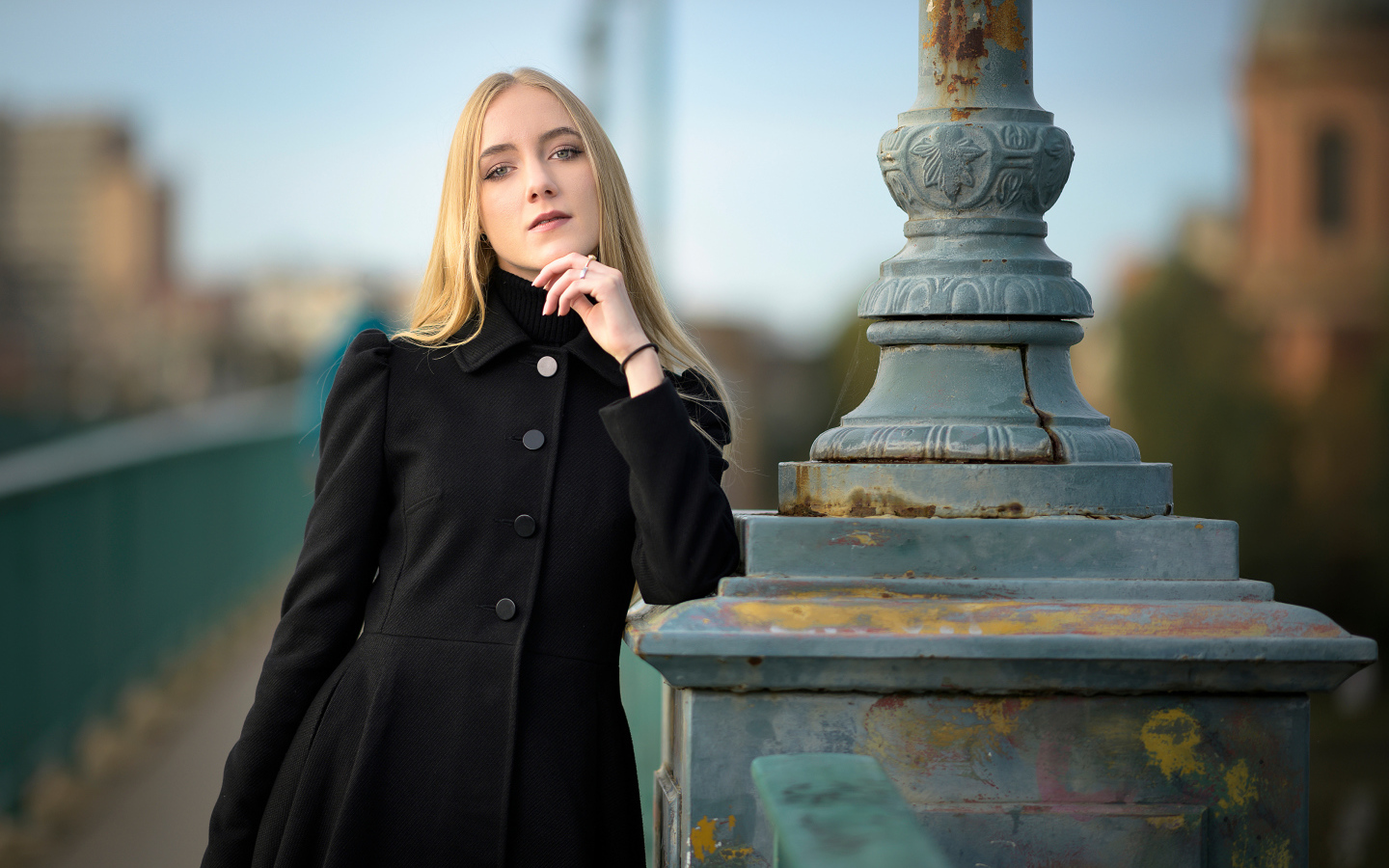 Красивая блондинка в черном пальто стоит у фонаря