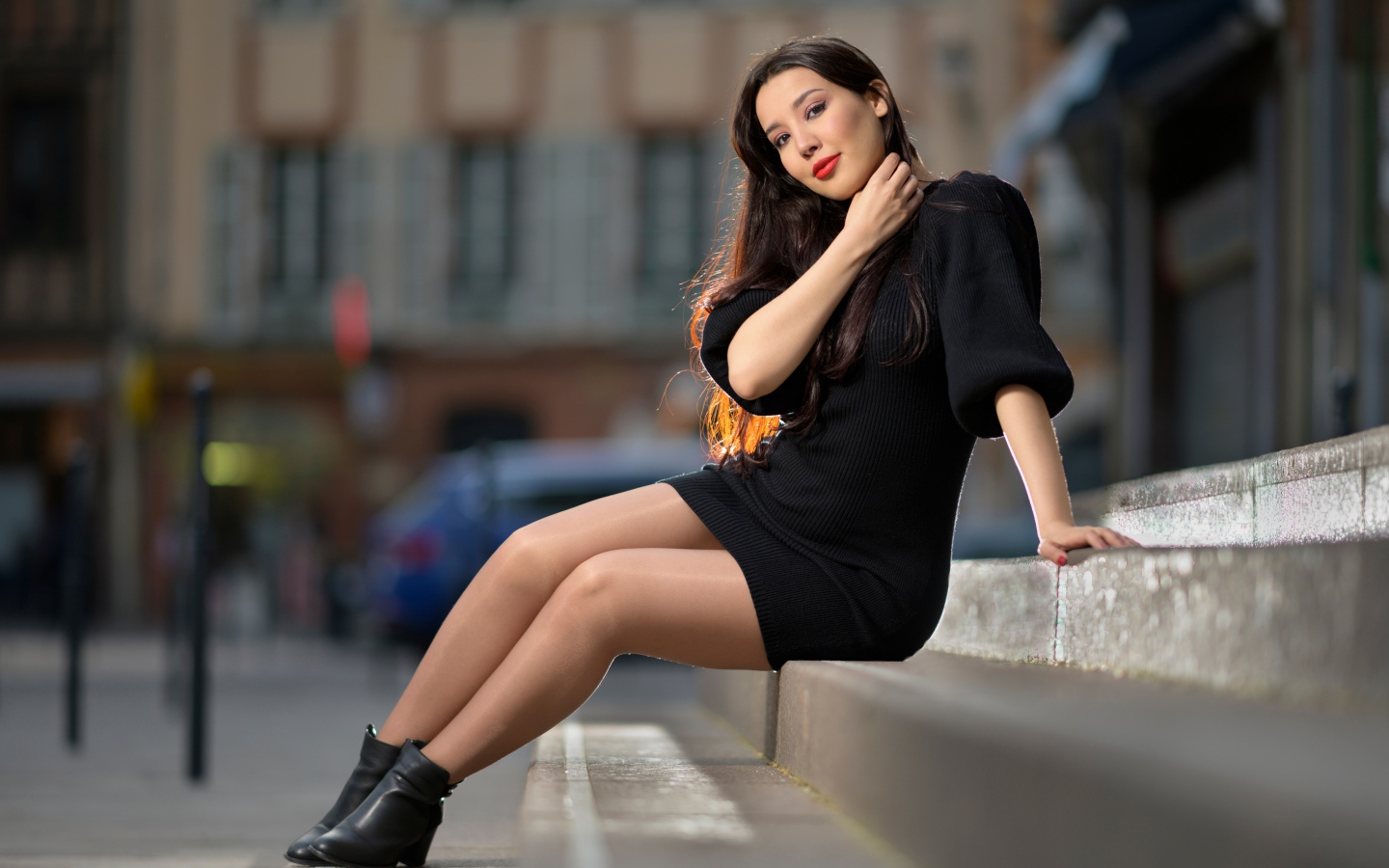 Красивая девушка в черном платье сидит на ступенях