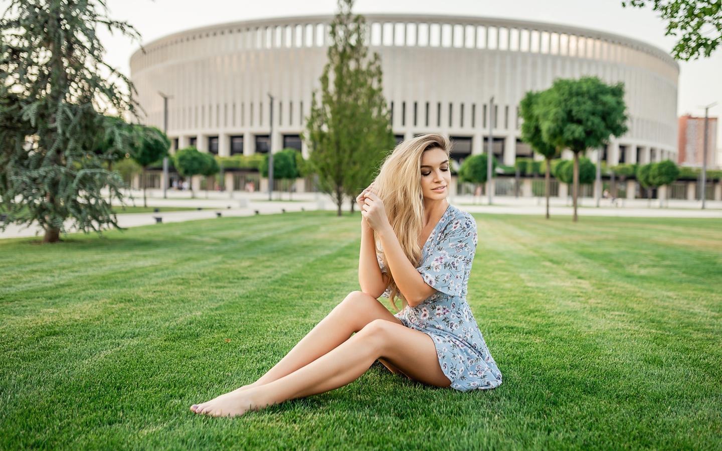 Красивая девушка в платье сидит на зеленом газоне 