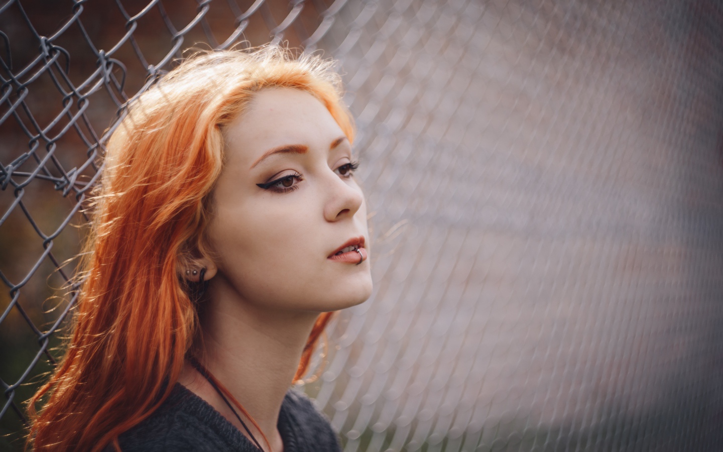 Красивая рыжеволосая девушка с пирсингом у железной сетки 