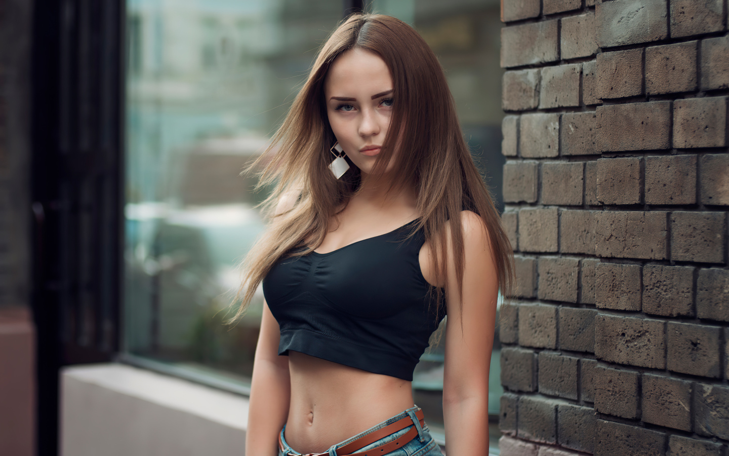 Красивая стройная девушка в черном топе стоит у стены