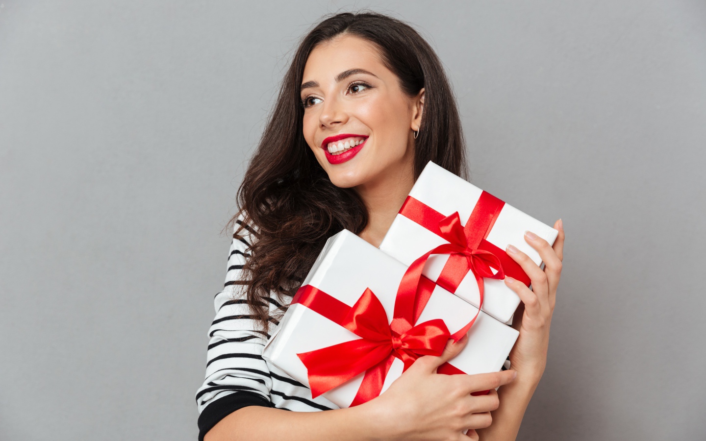 Красивая улыбающаяся девушка с подарками в руках на сером фоне 