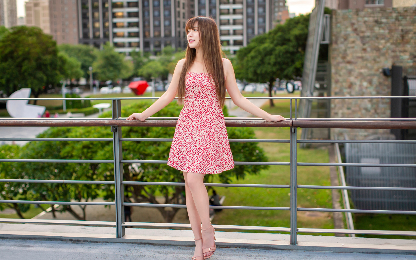 Милая девушка азиатка в платье стоит у перил 