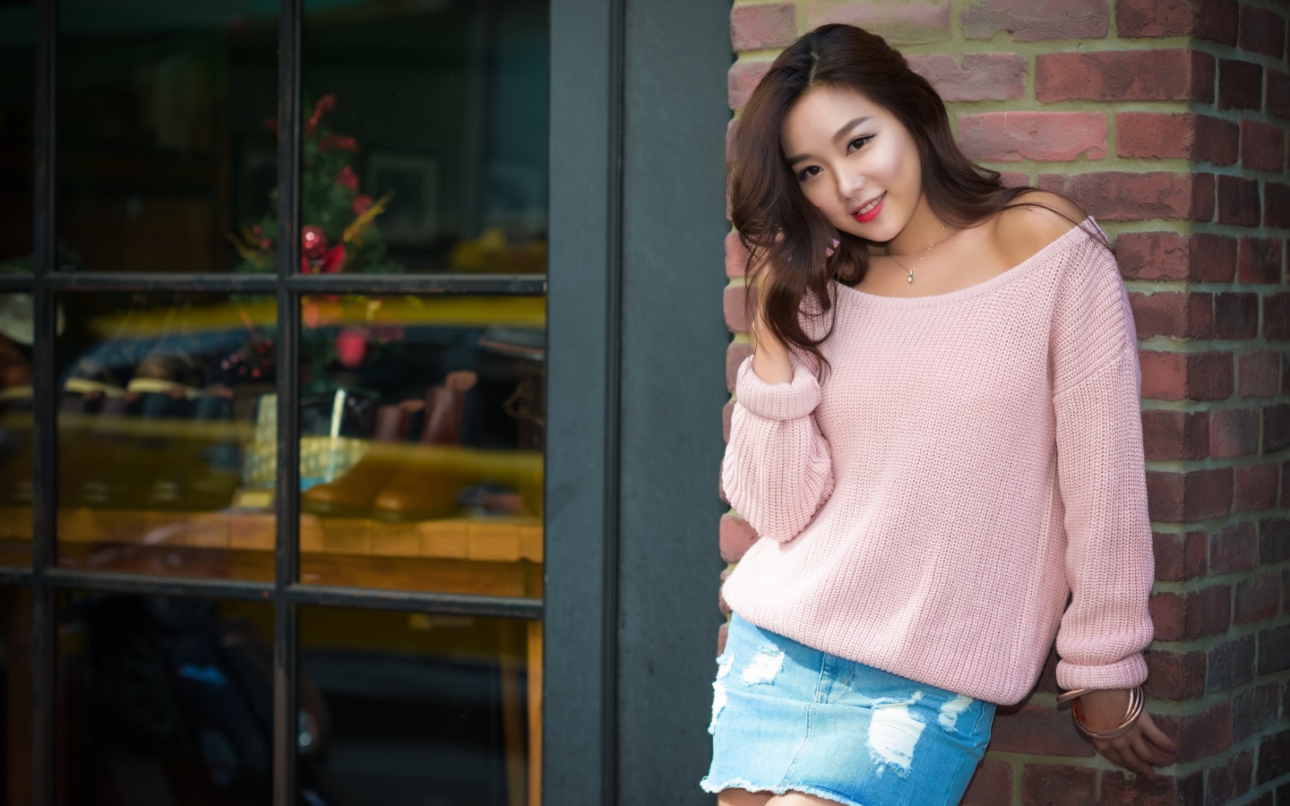 Милая азиатка в розовом свитере стоит у стены 