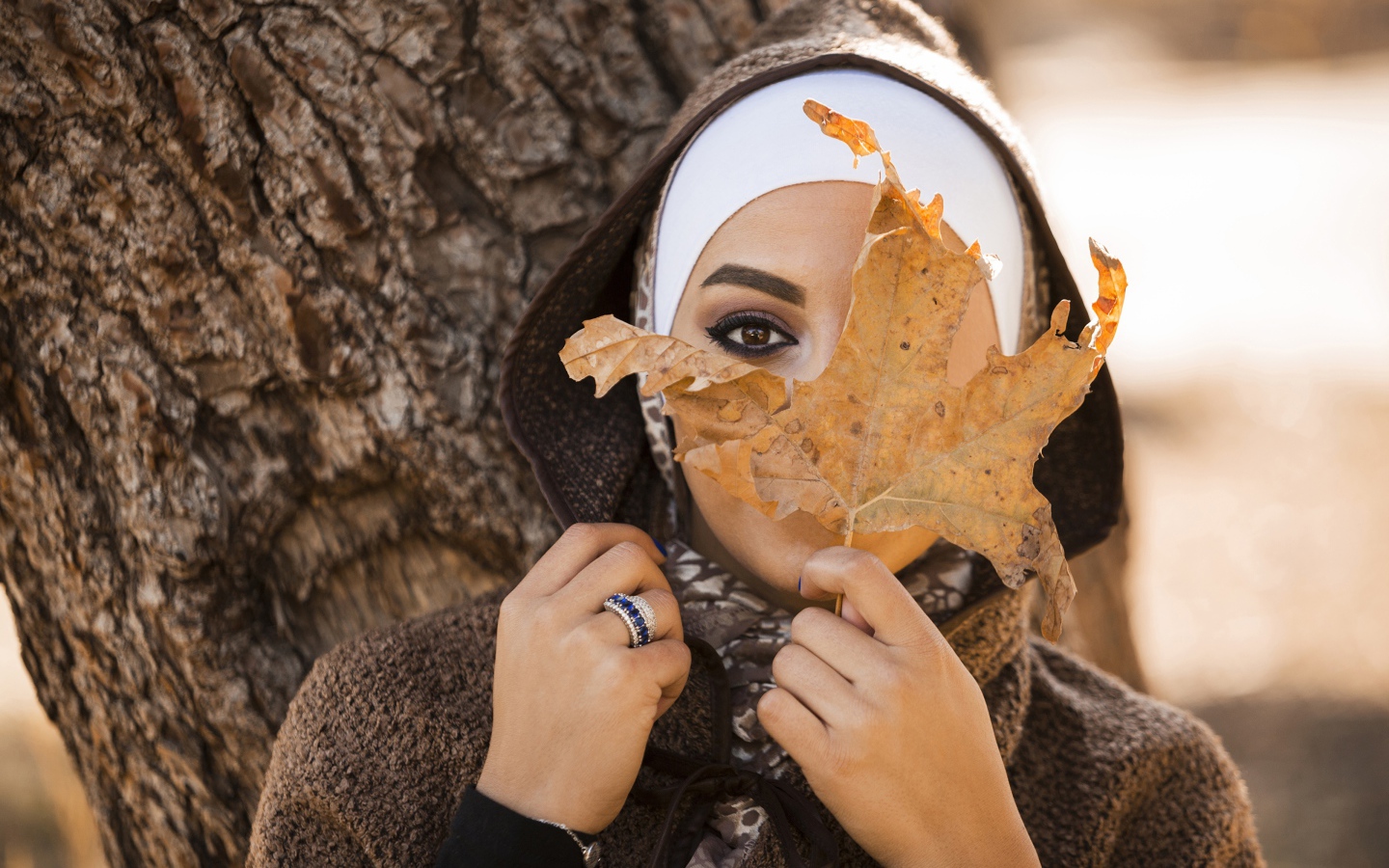 Девушка в пальто с закрывает лицо листом