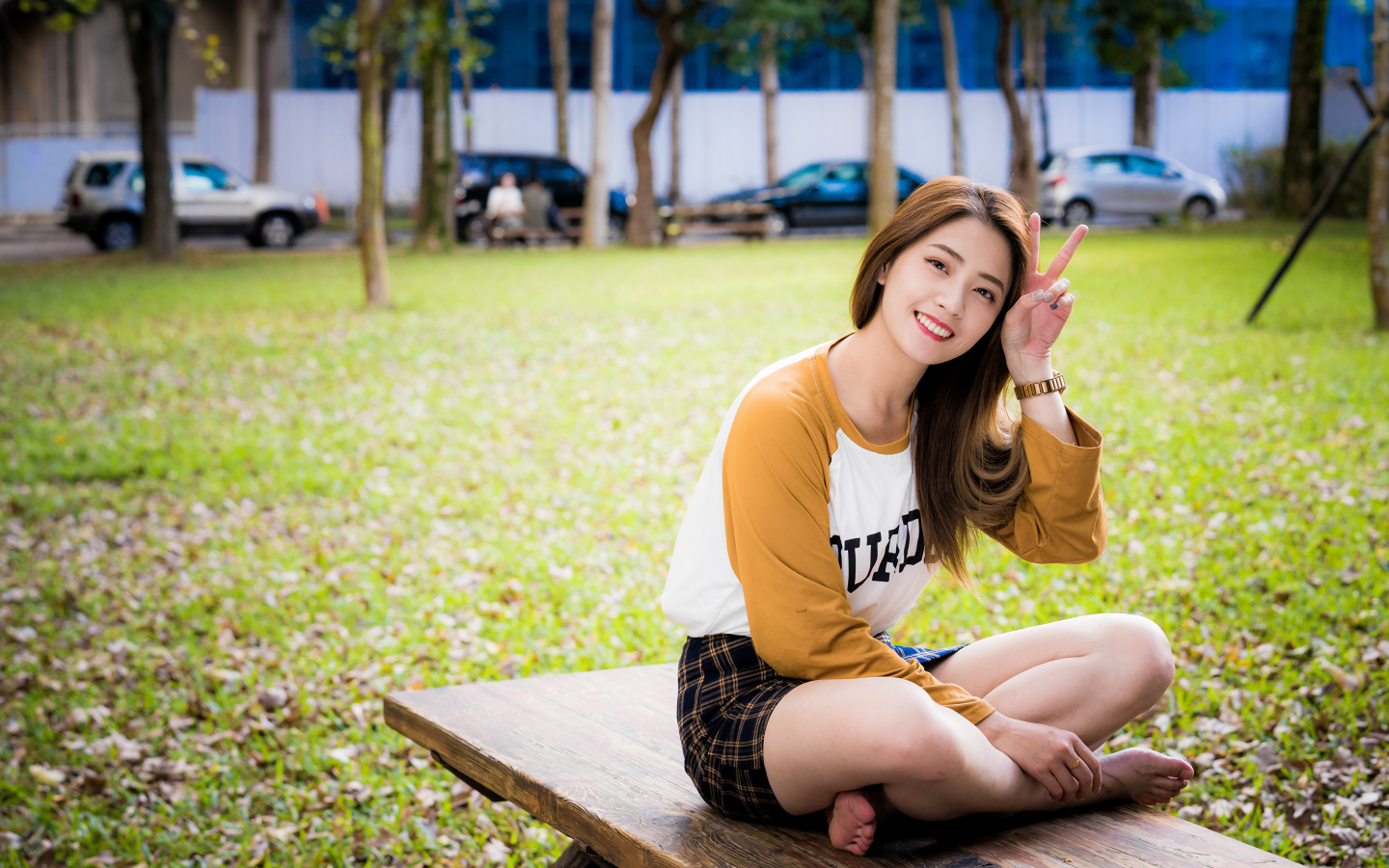 Улыбающаяся девушка азиатка сидит на лавке в парке 