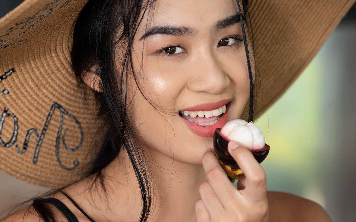 Улыбающаяся азиатка в шляпе с фруктом в руке