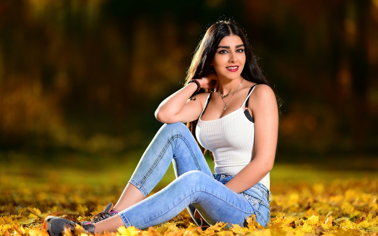Улыбающаяся брюнетка сидит на опавшей листве