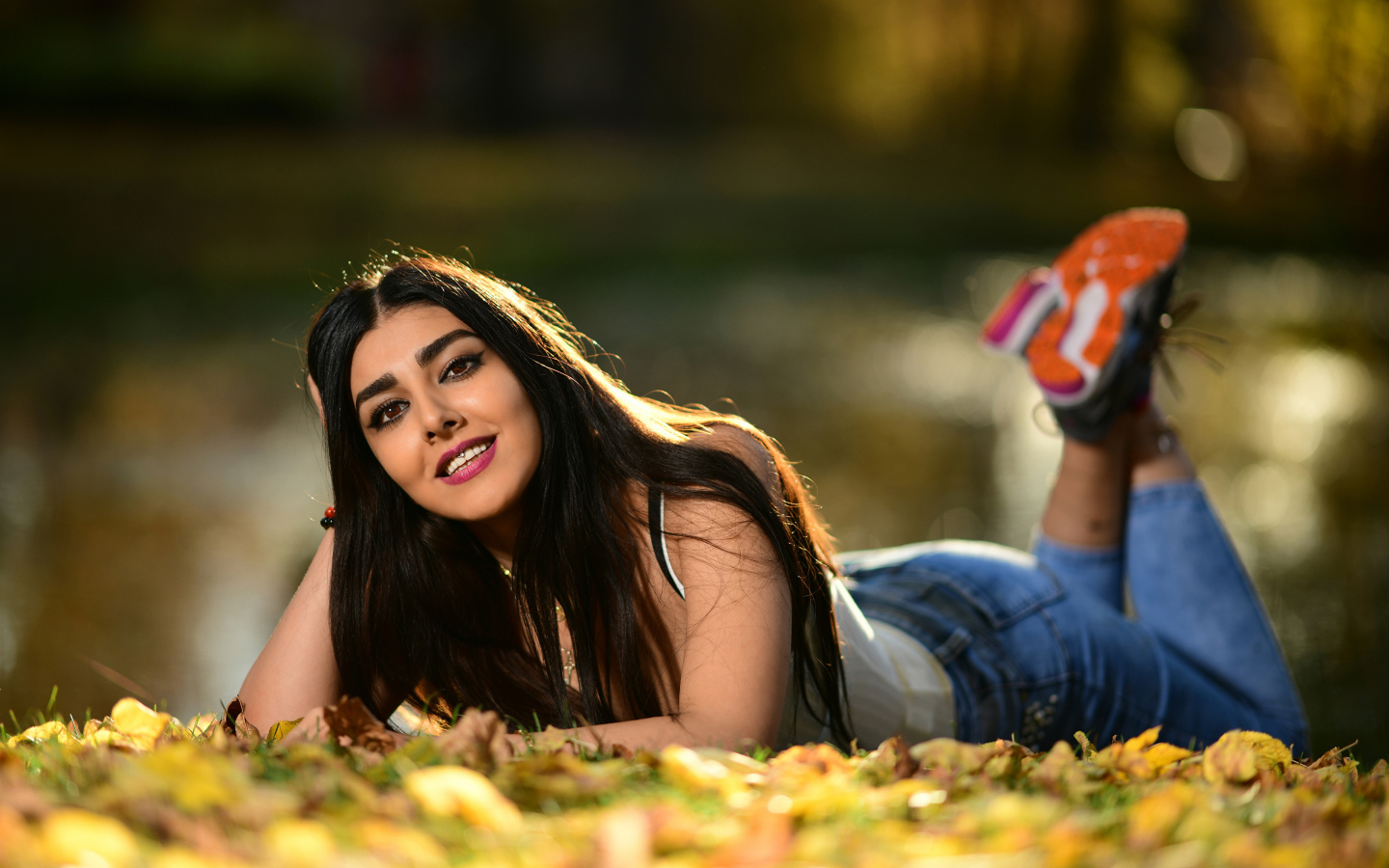 Улыбающаяся девушка модель лежит на земле с опавшими листьями