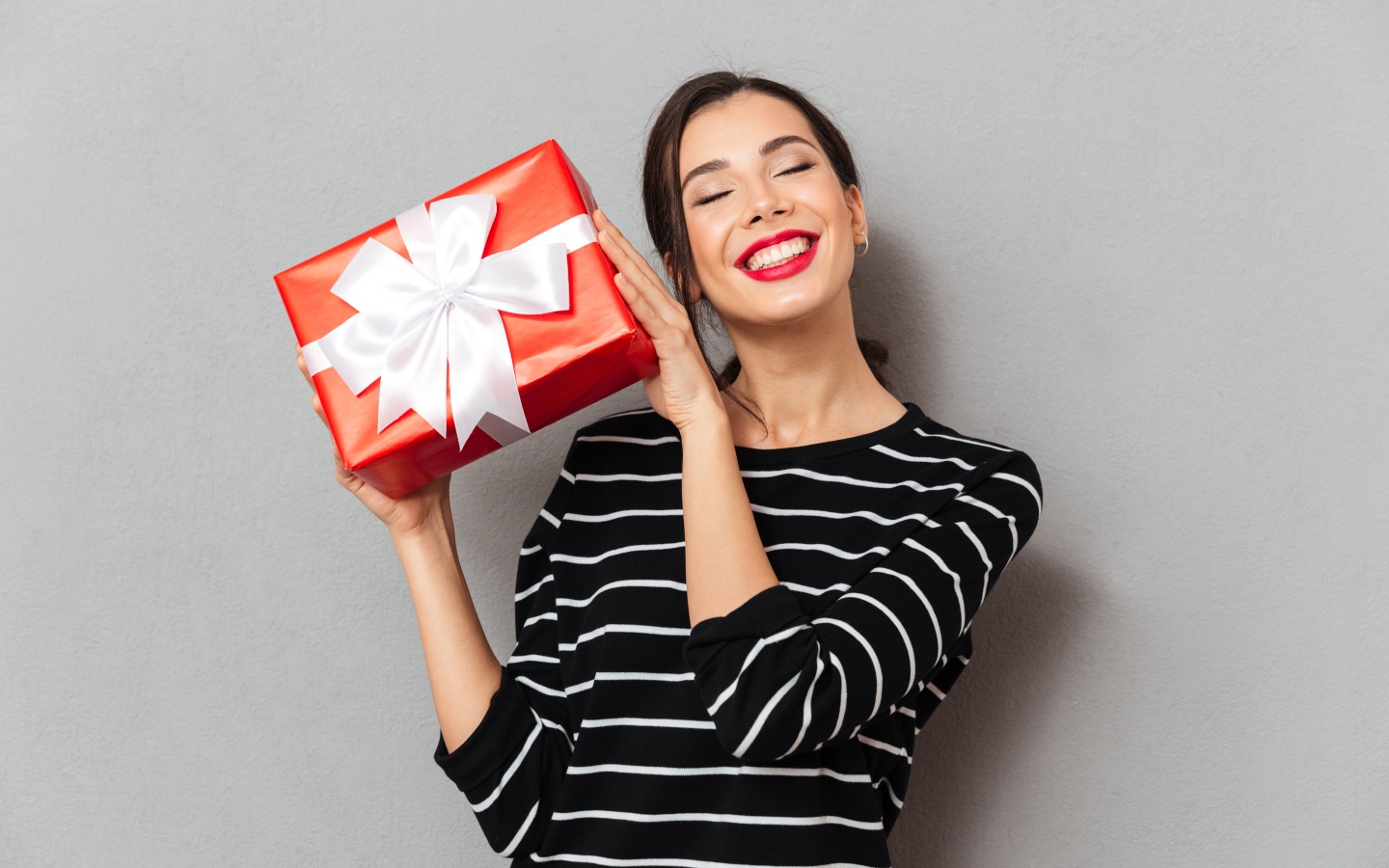 Улыбающаяся девушка с подарком в руках на сером фоне 