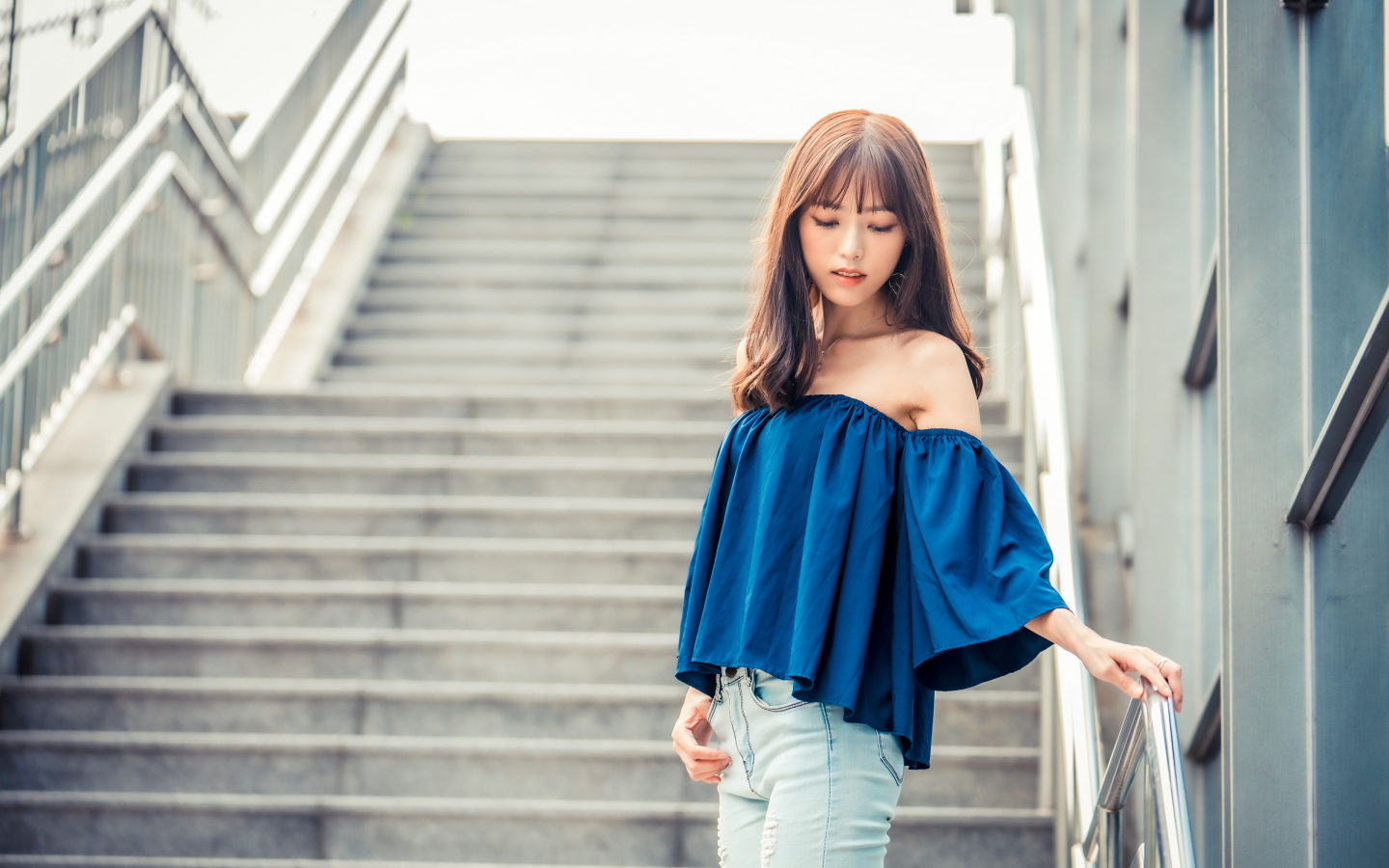Стильная девушка азиатка с опущенной головой стоит на ступеньках 