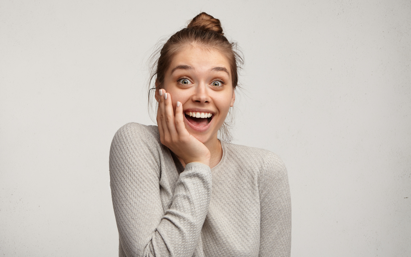 Удивленная девушка с рукой у лица на сером фоне 