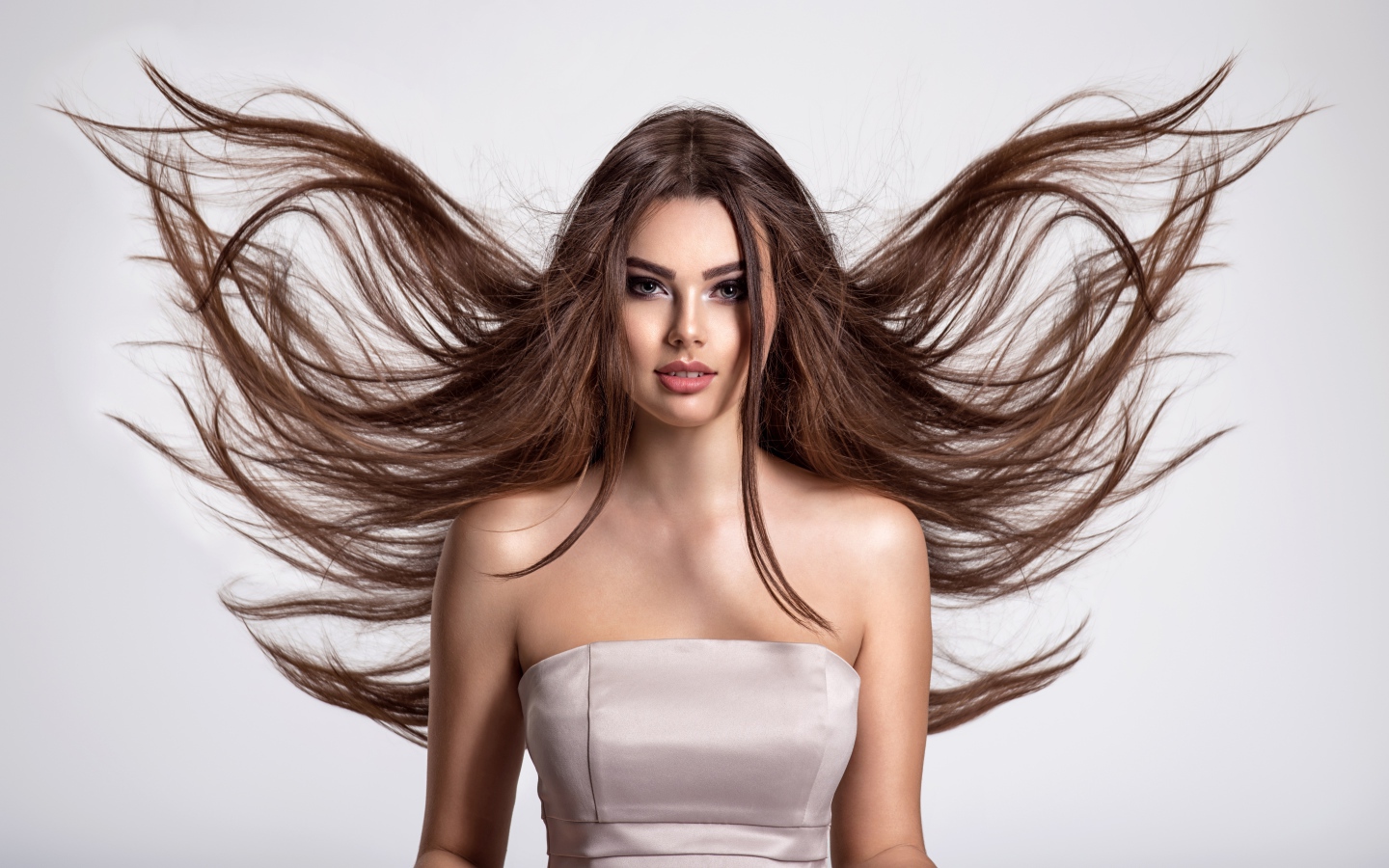 Ветер развивает волосы красивой девушке шатенке на сером фоне