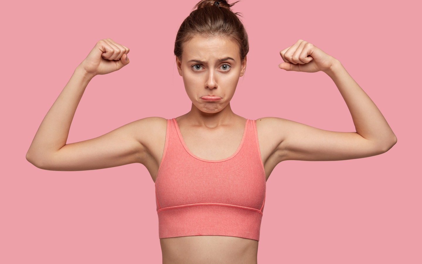 Расстроенная девушка без накаченных рук на розовом фоне