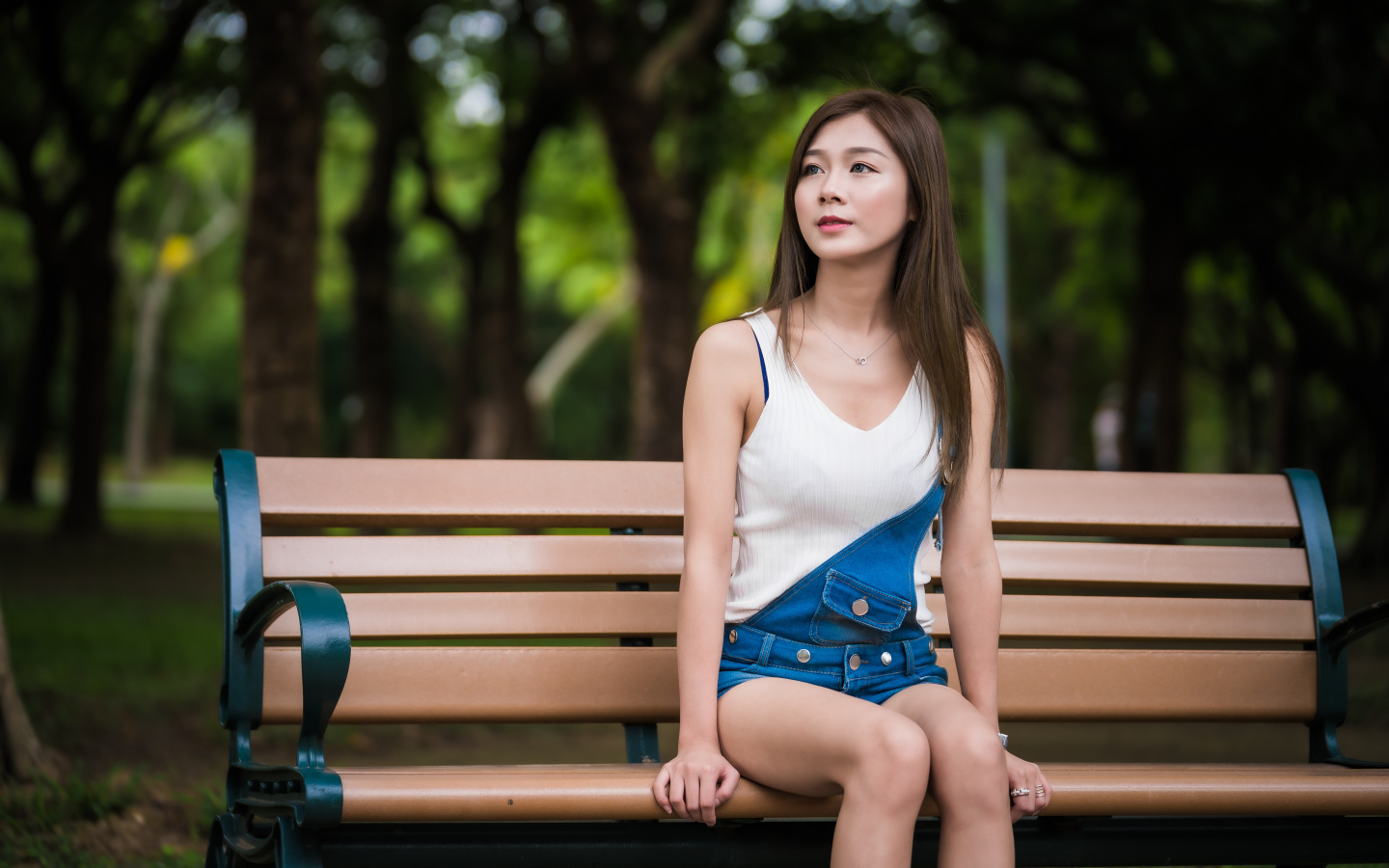 Молодая девушка азиатка сидит в парке на лавочке