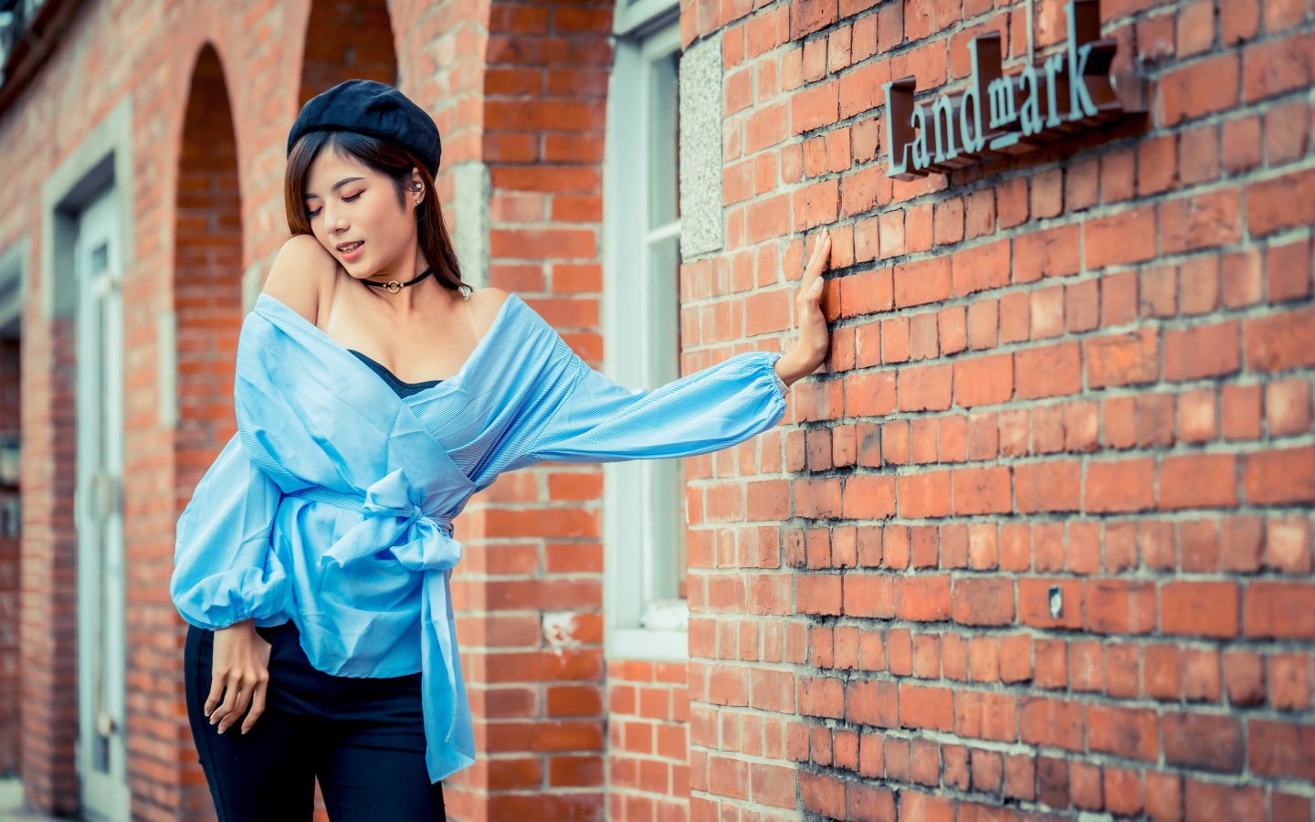 Молодая азиатка в черном берете стоит у стены 