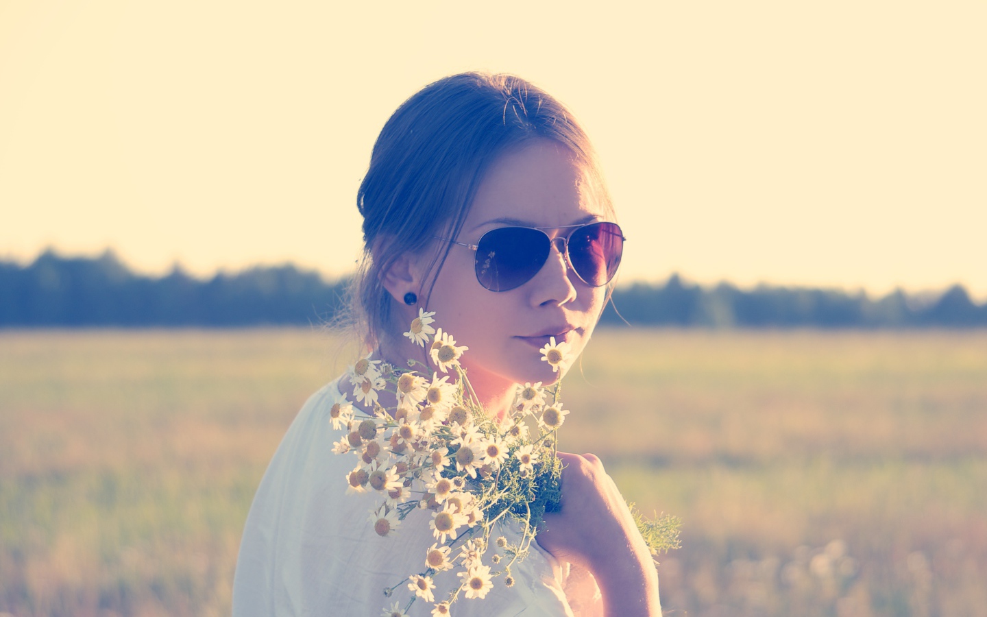 Молодая девушка в солнечных очках с букетом ромашек на поле