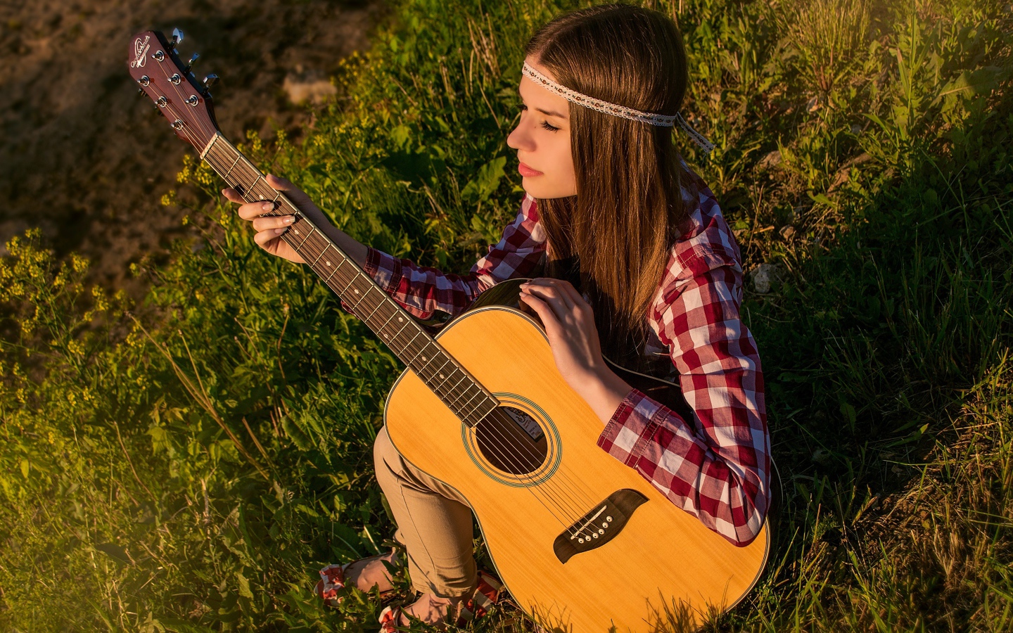Молодая девушка хиппи сидит с гитарой на траве 