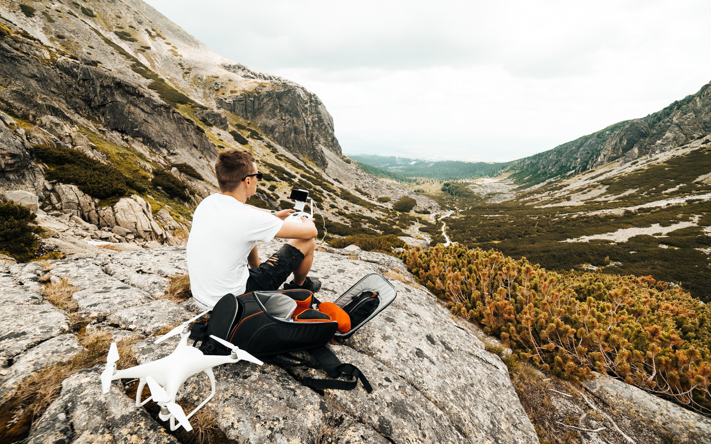 Парень с квадрокоптером сидит на камне в горах 