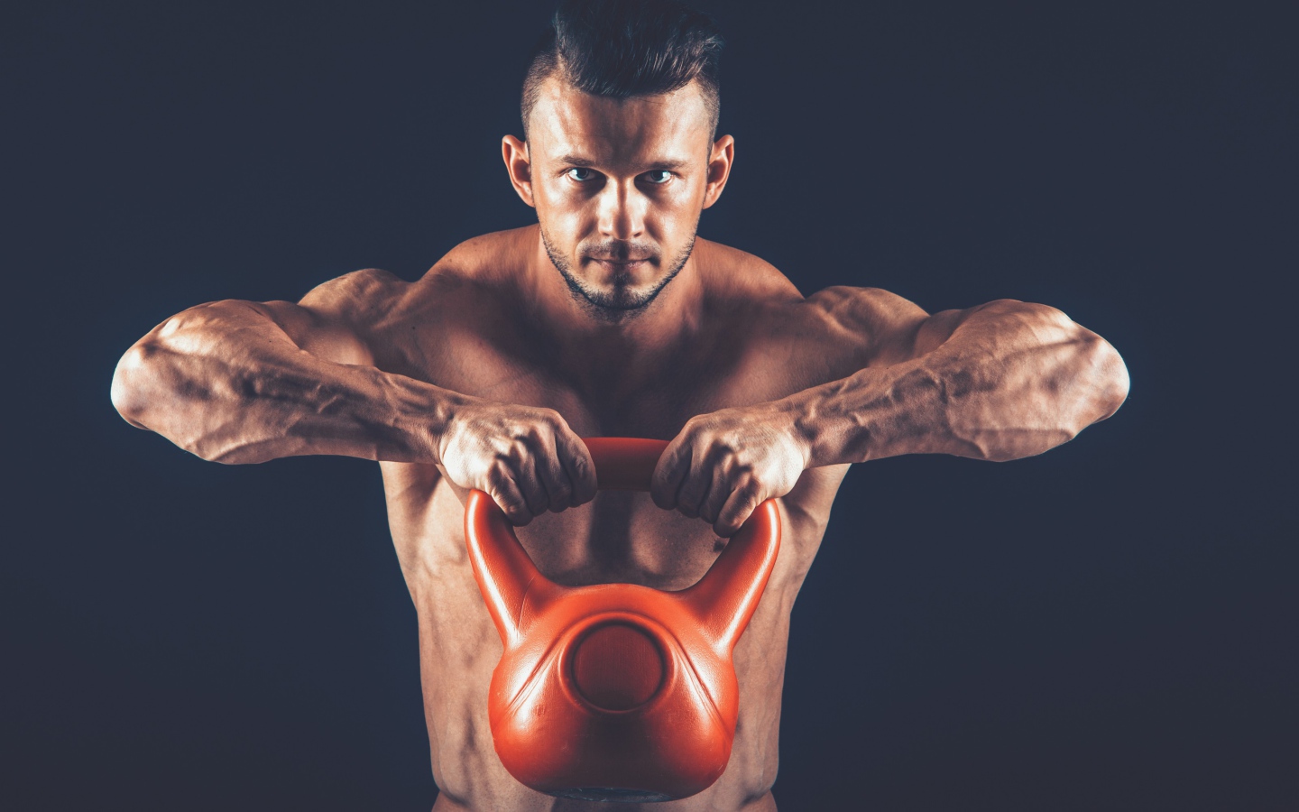 Накаченный парень поднимает тяжелую гирю на черном фоне