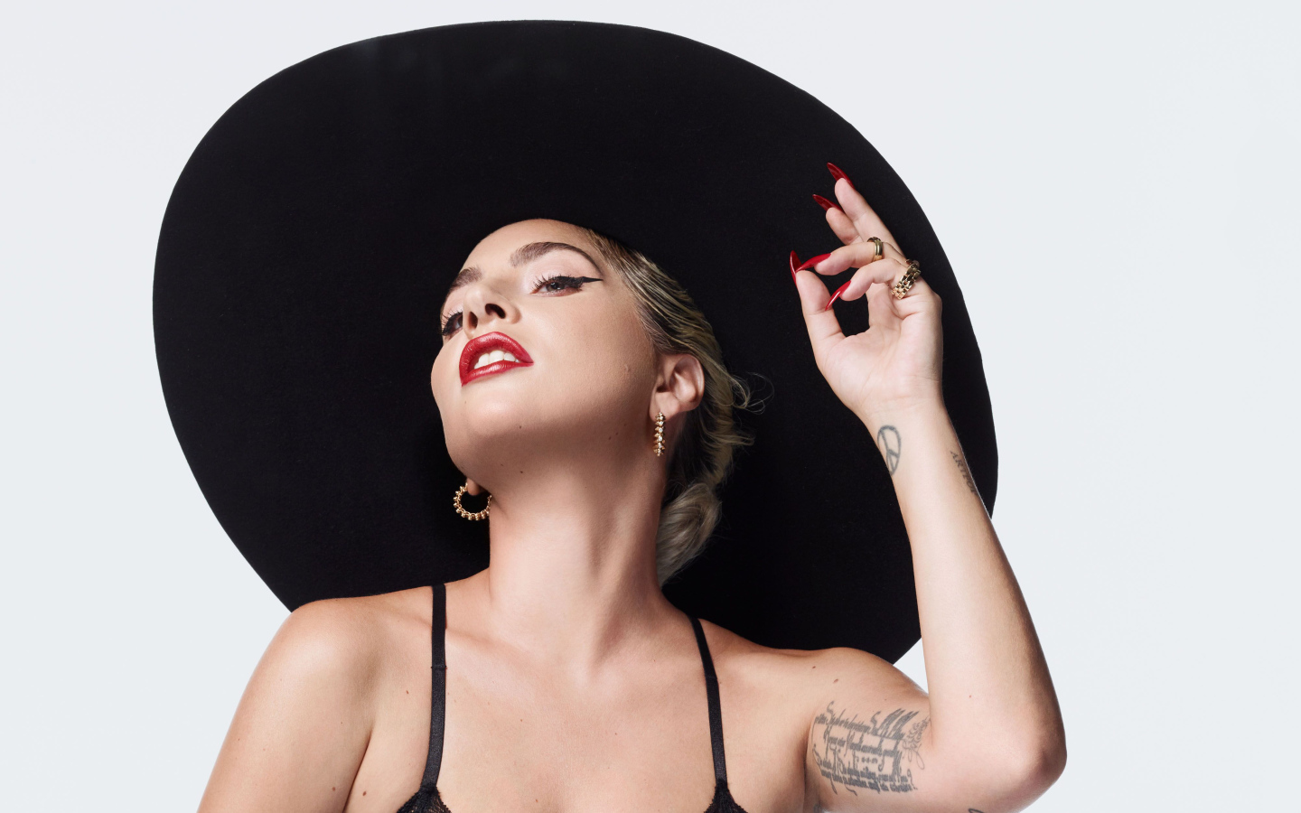 Певица Леди Гага в большой черной шляпе на белом фоне