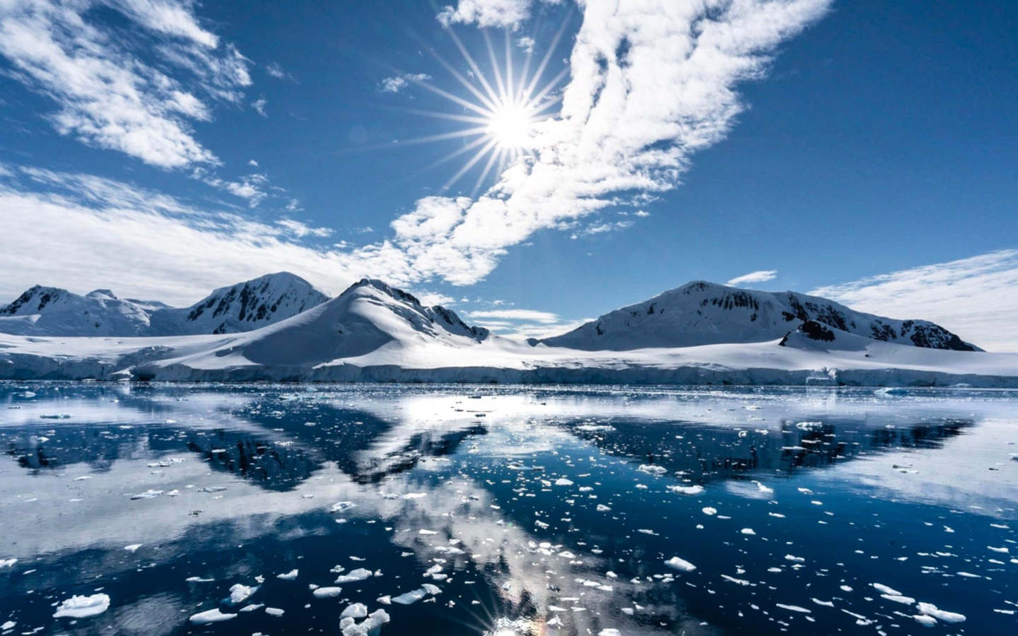 Белые облака в солнечном небе отражаются в озере у заснеженных гор 