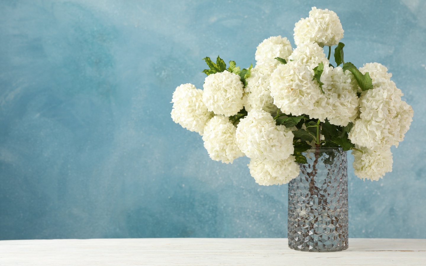 Белые цветы гортензии в стеклянной вазе на столе 