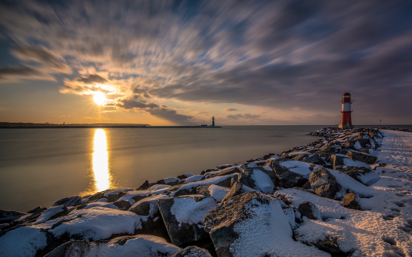 Заснеженные камни на берегу моря с маяком на закате