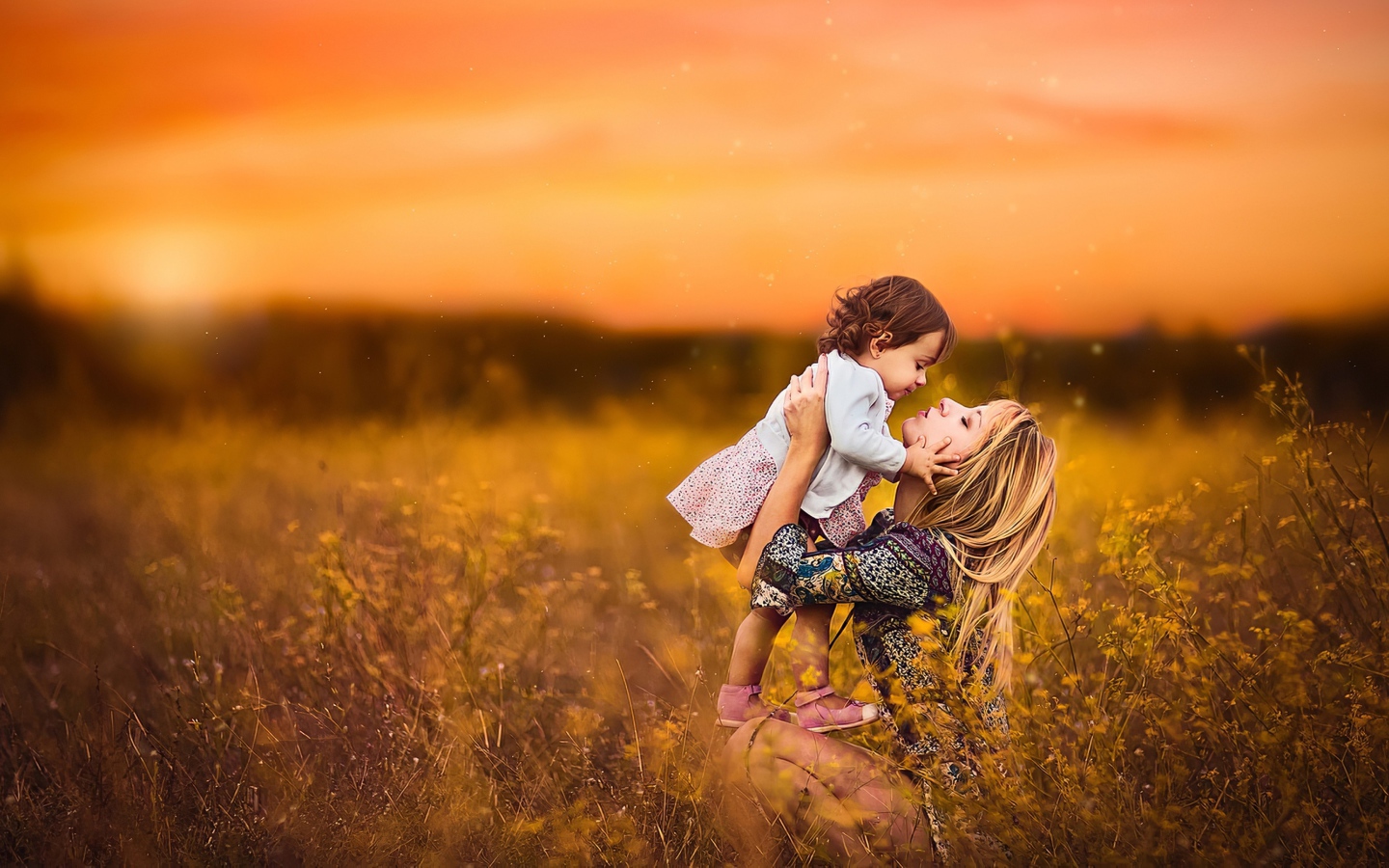 Девушка держит маленькую девочку на руках в поле на закате