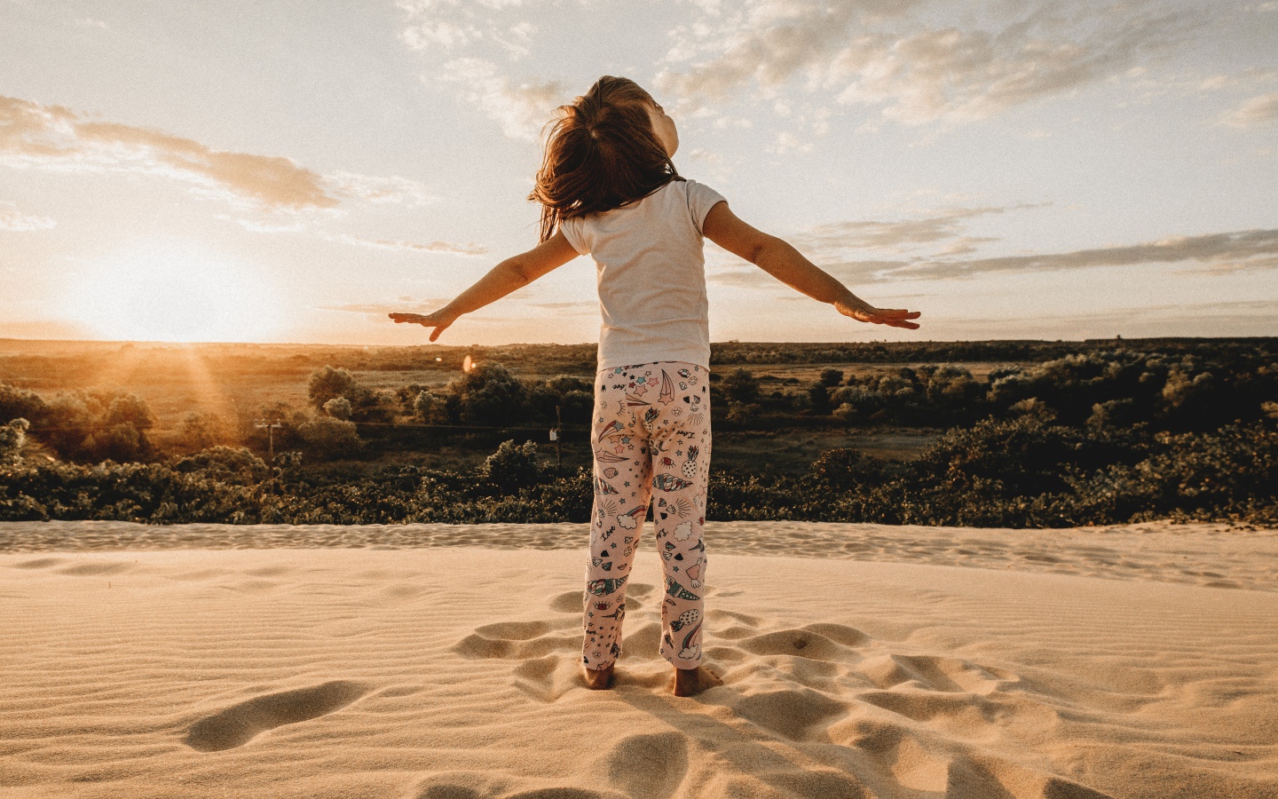 Маленькая девочка стоит на песку в лучах солнца