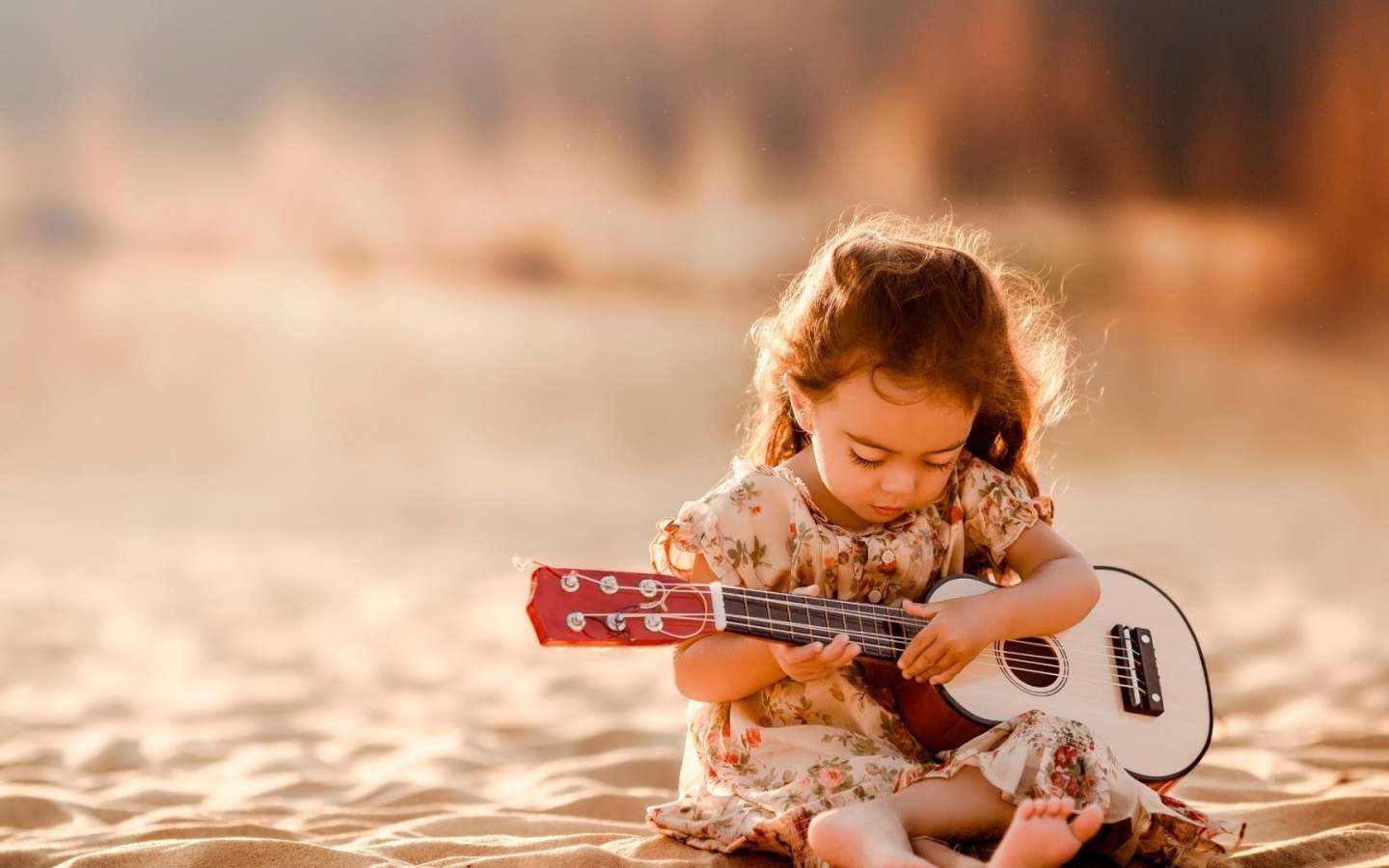 Маленькая девочка с гитарой сидит на песке 