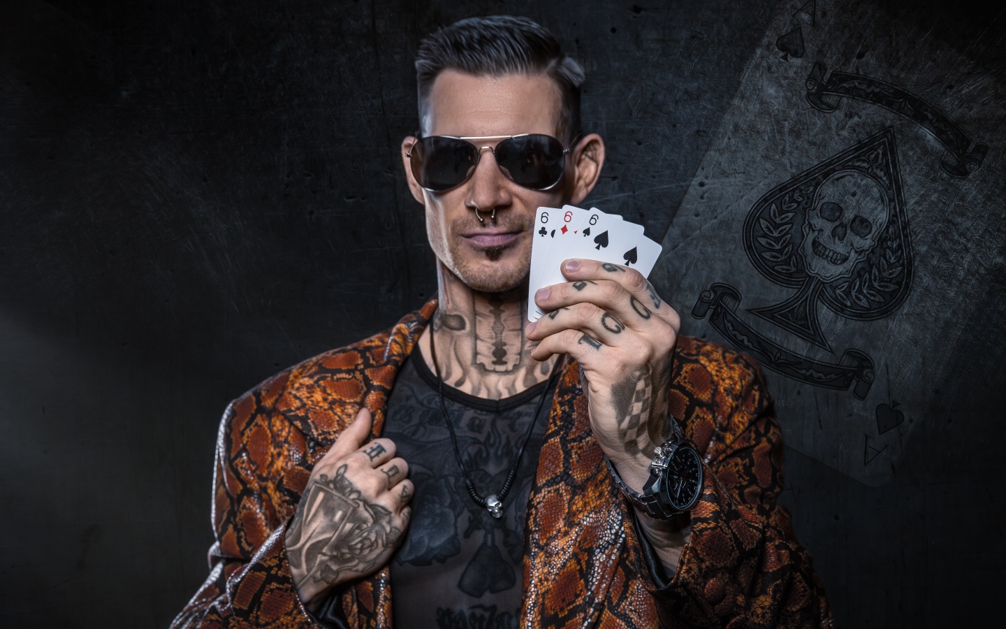 Мужчина с татуировками на теле держит в руке три карты шестерки 