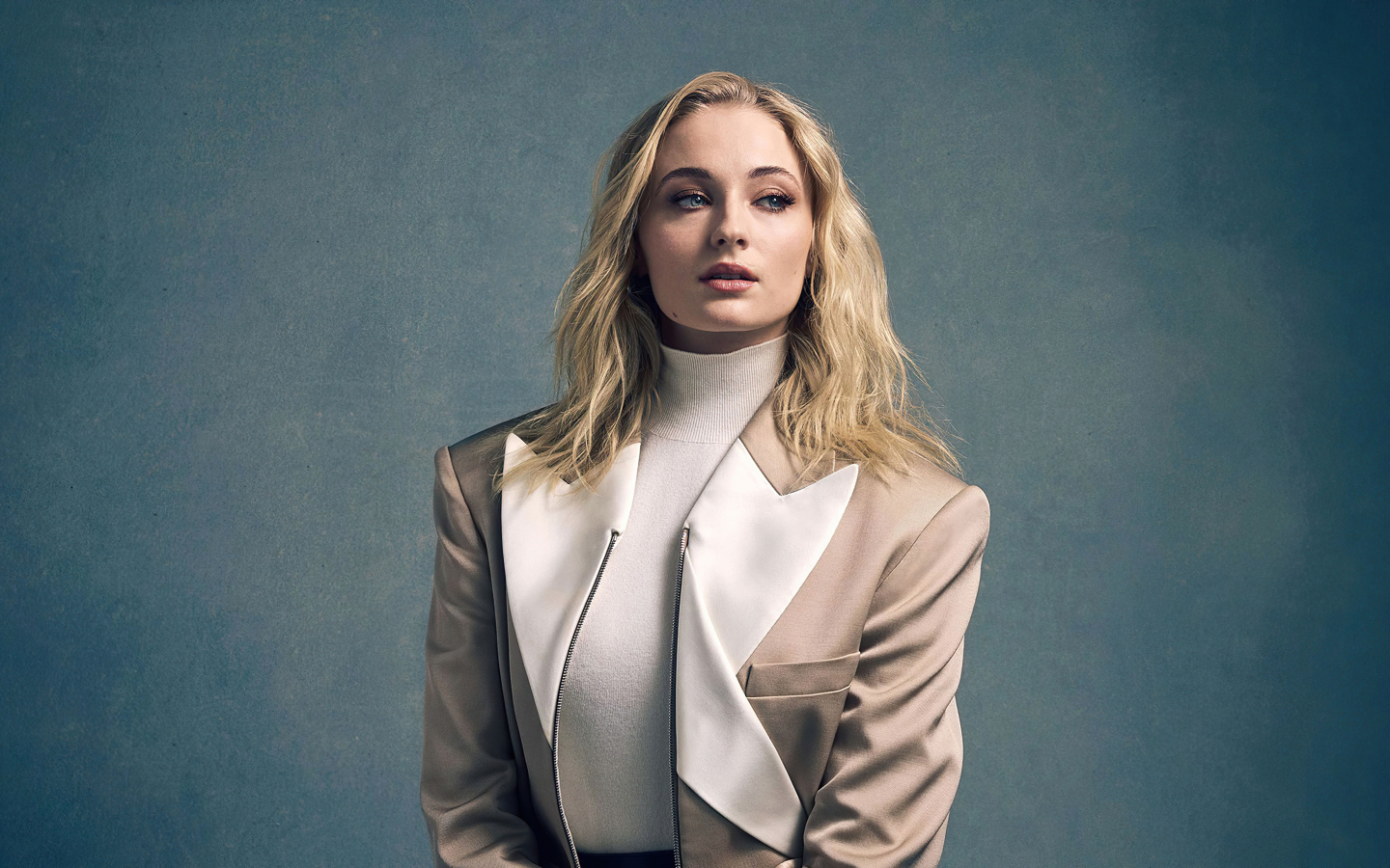Actress Sophie Turner in a suit on a gray background