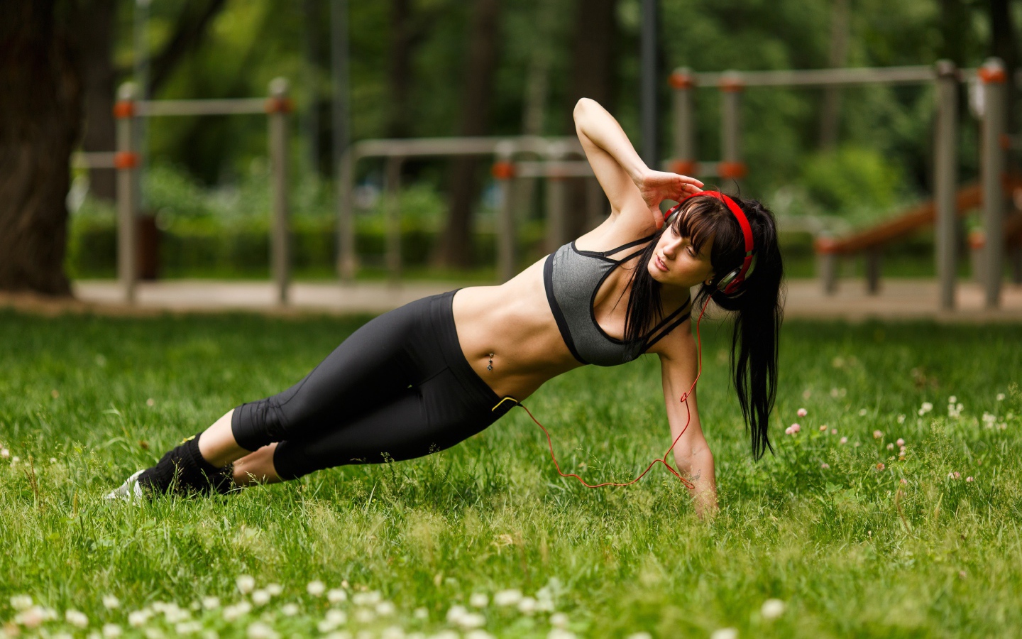 Девушка с наушниками на голове занимается фитнесом на траве 