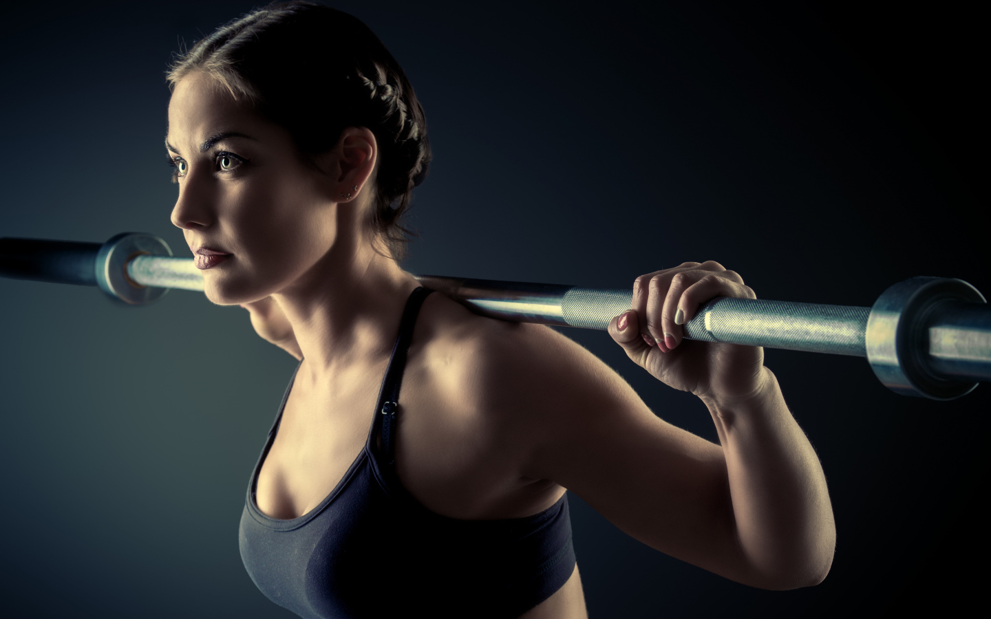 Спортивная девушка занимается со штангой в спортзале на сером фоне