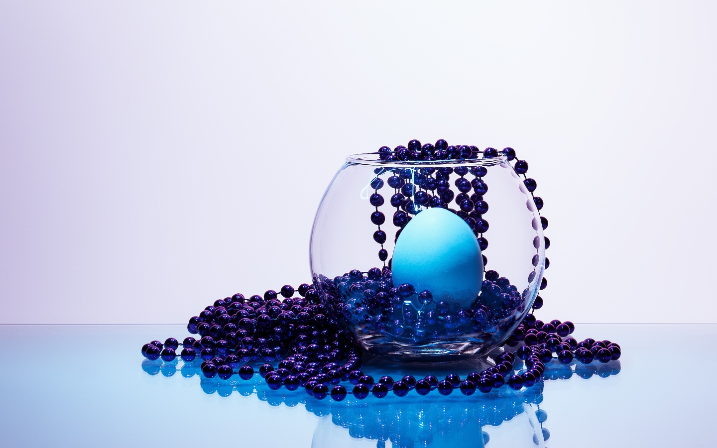 Синие бусы на столе со стеклянной вазой и яйцом
