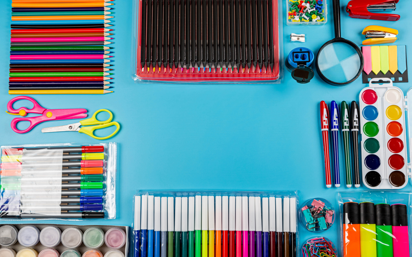 Много разноцветных канцелярских предметов на голубом фоне 