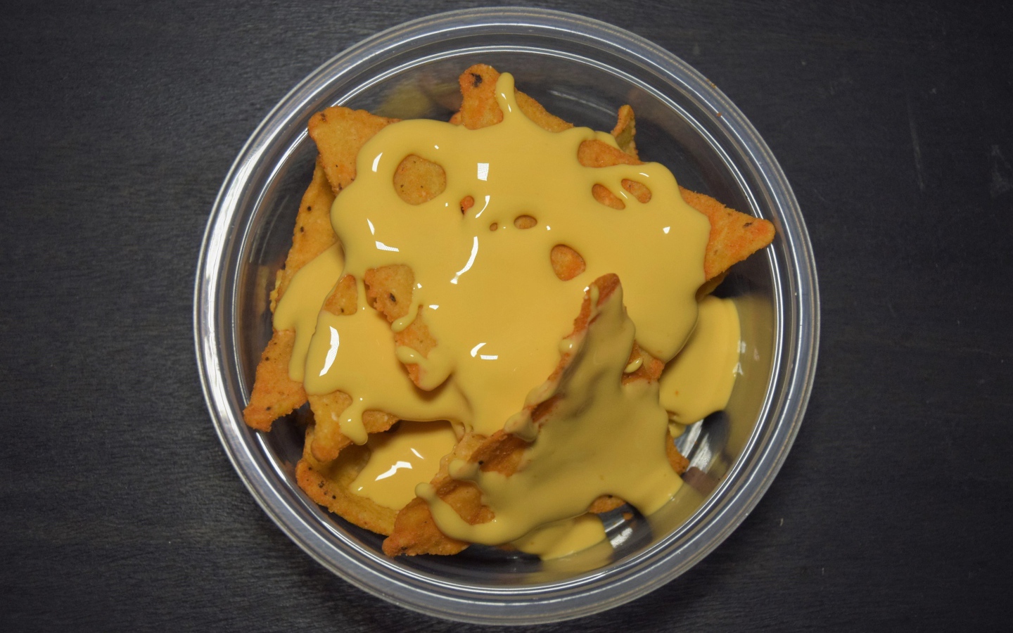 Чипсы начос с сырным соусом в миске на черном фоне