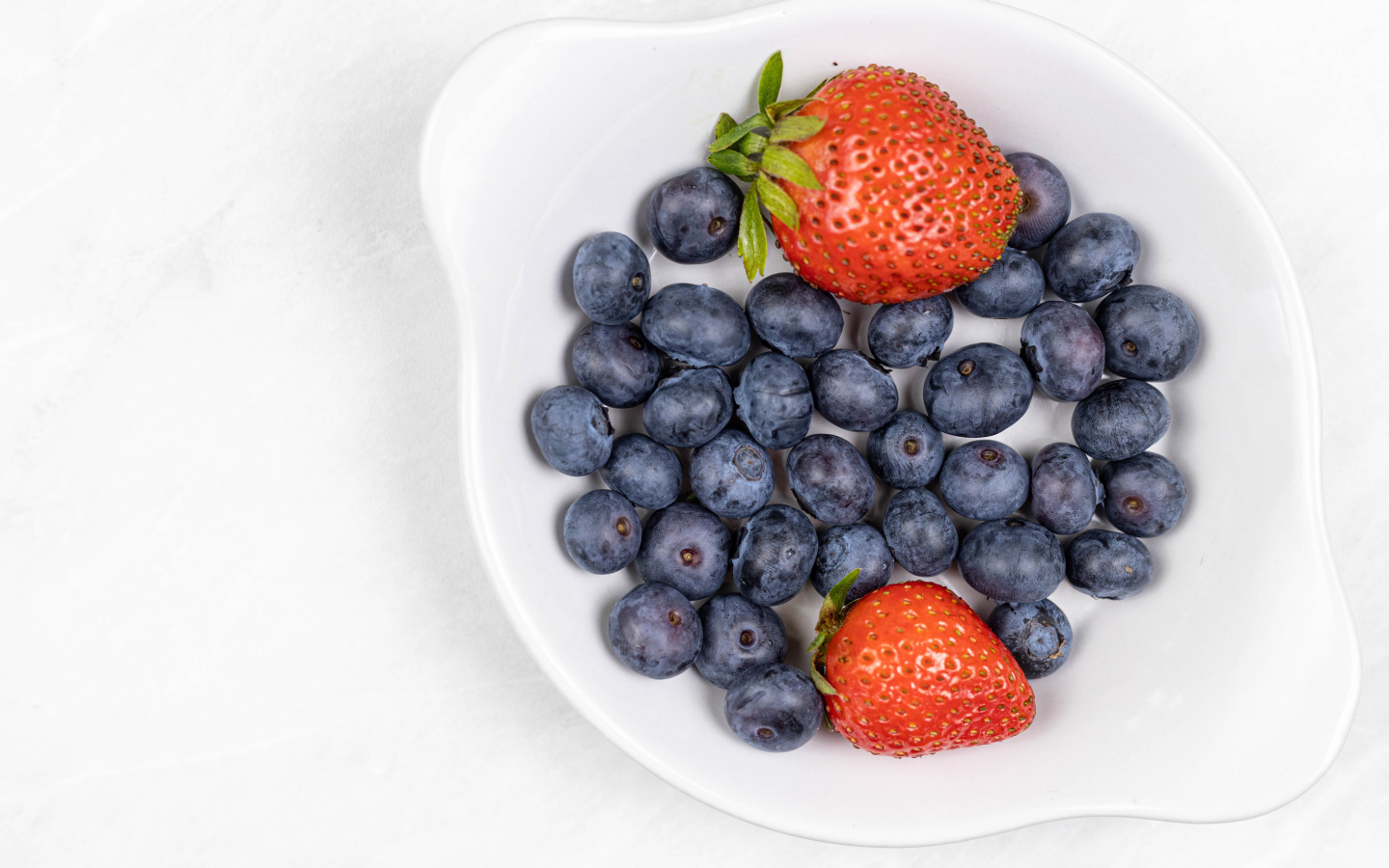 Много синей черники с клубникой в белой тарелке 