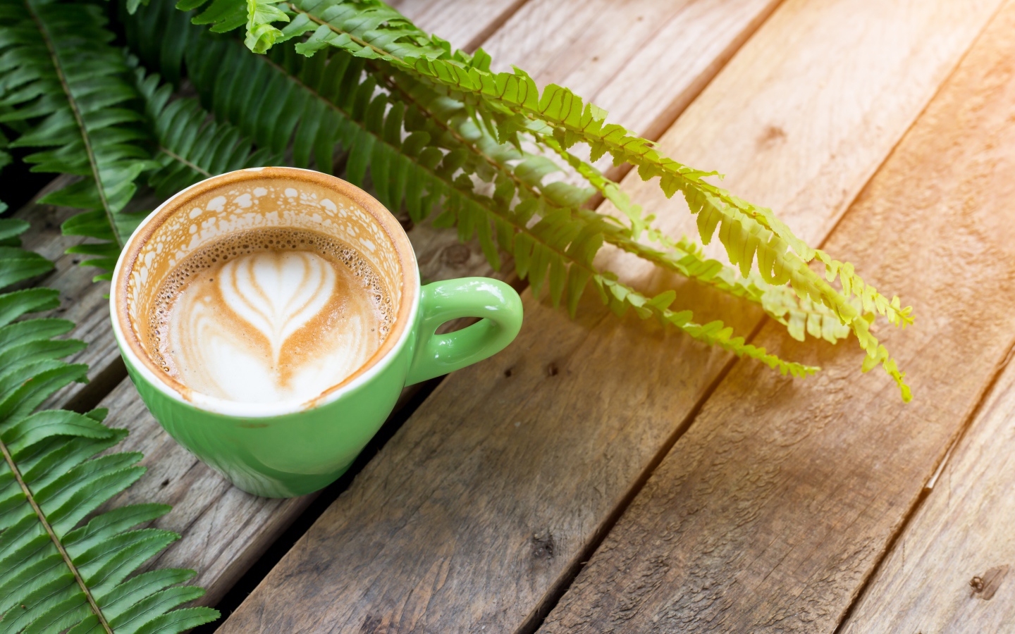 Чашка вкусного капучино  на столе с листьями папоротника
