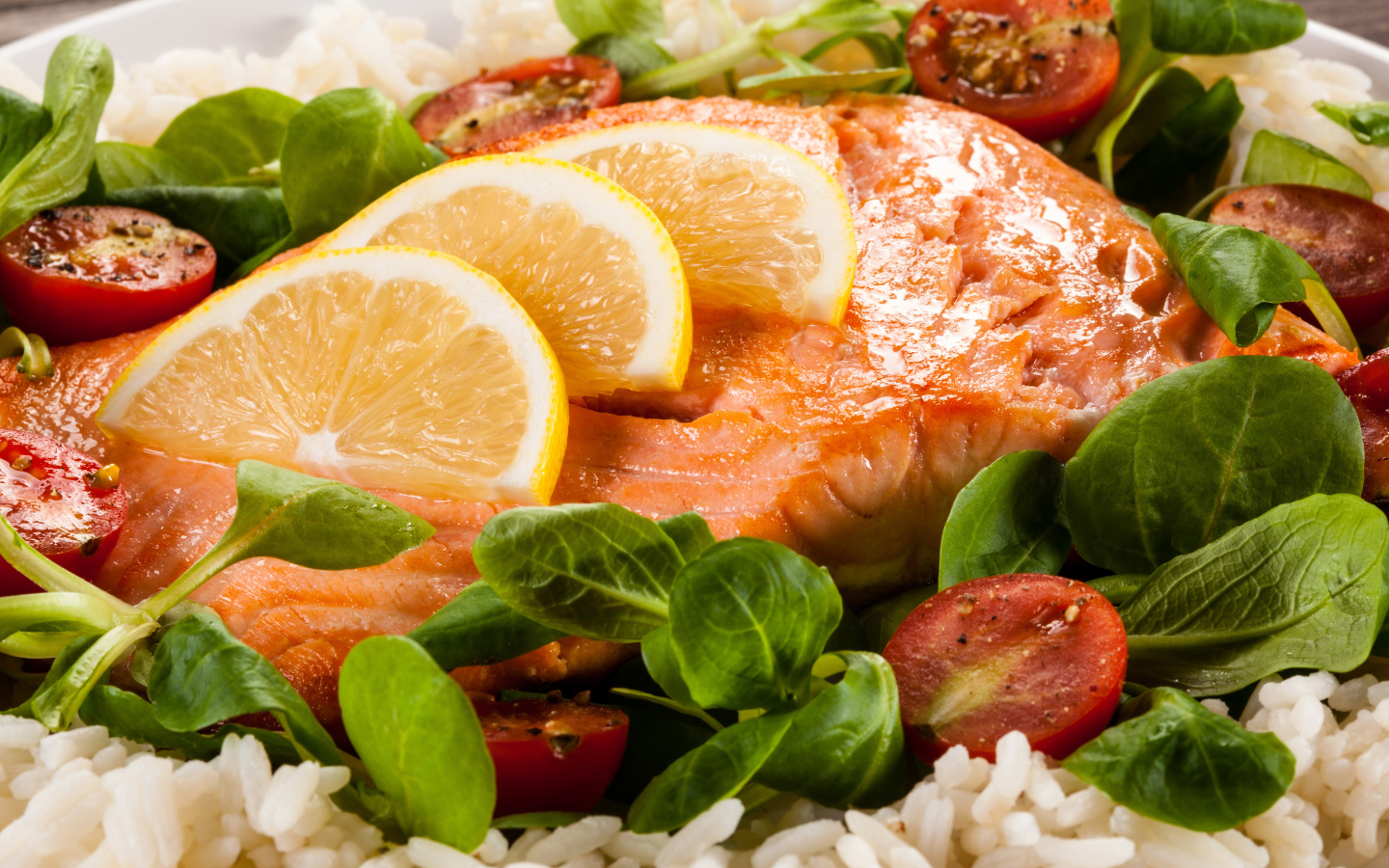 Кусок запеченной красной рыбы на тарелке с лимоном, рисом, базиликом и помидорами