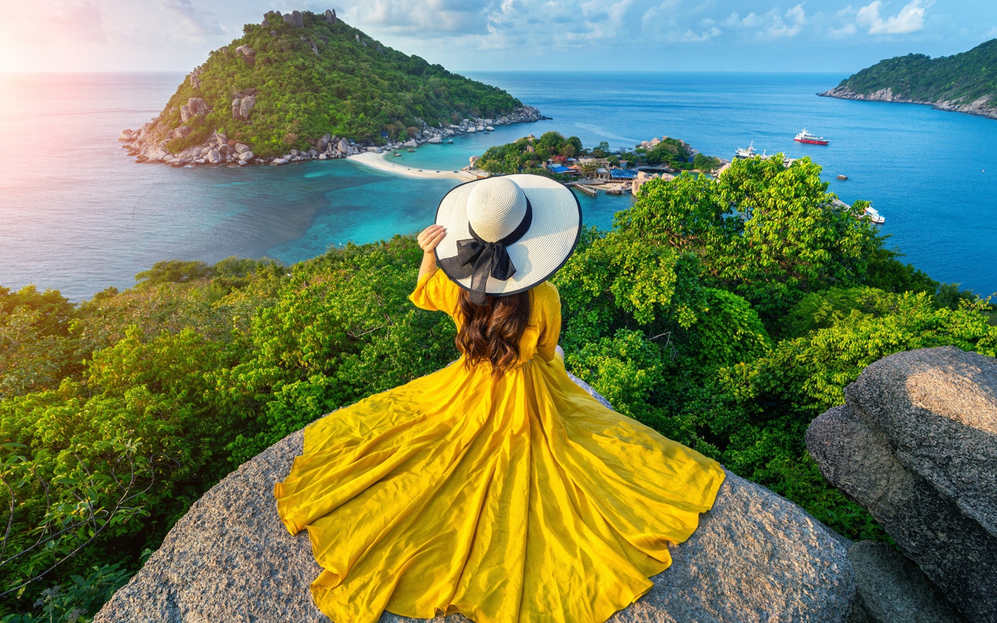 Девушка в красивом желтом платье сидит на камне с видом на море