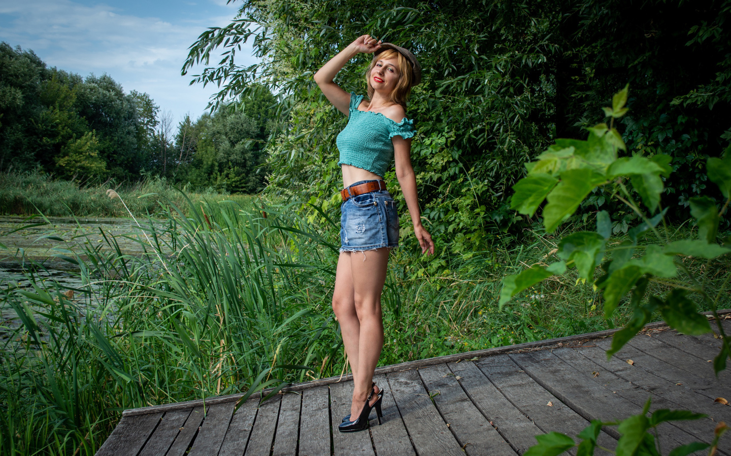 Красивая девушка в джинсовой юбке у пруда 