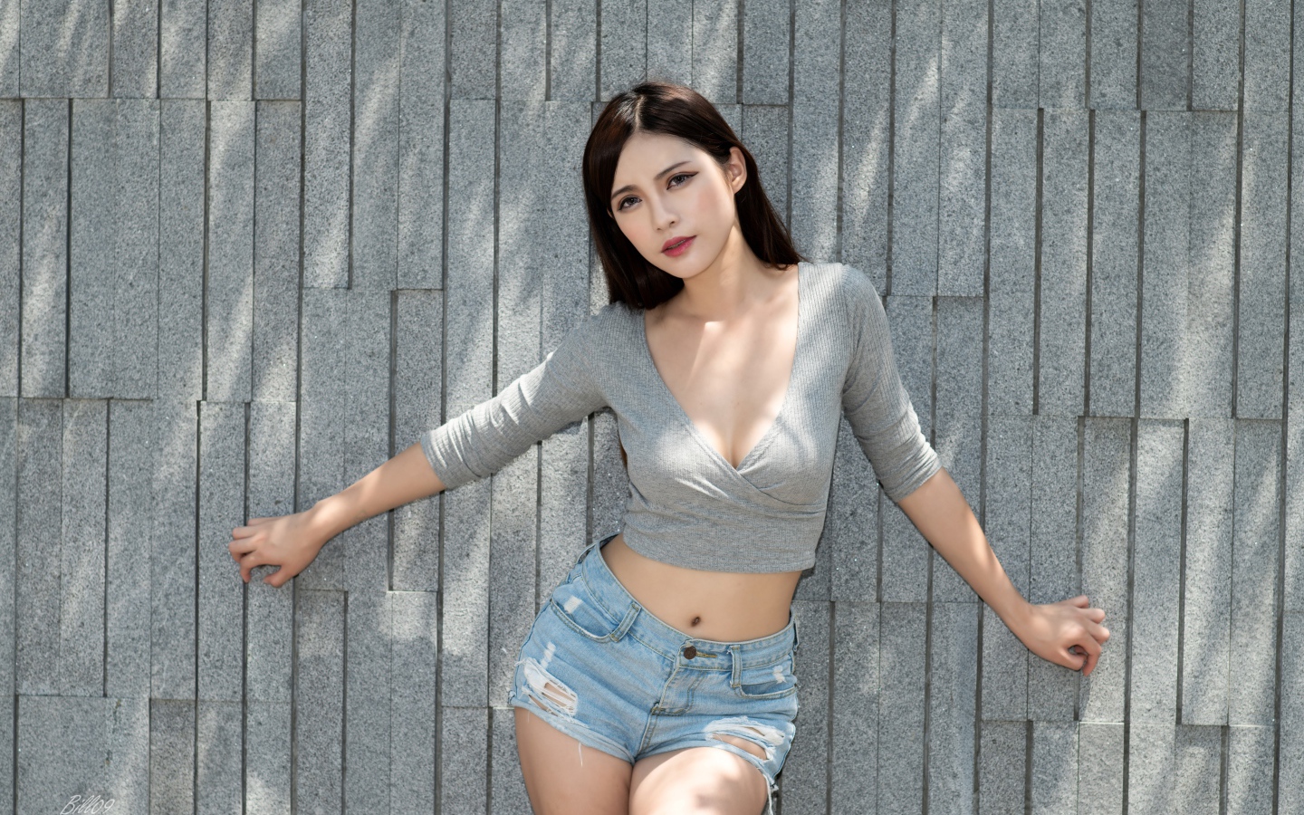 Милая девушка в серой кофте у стены 