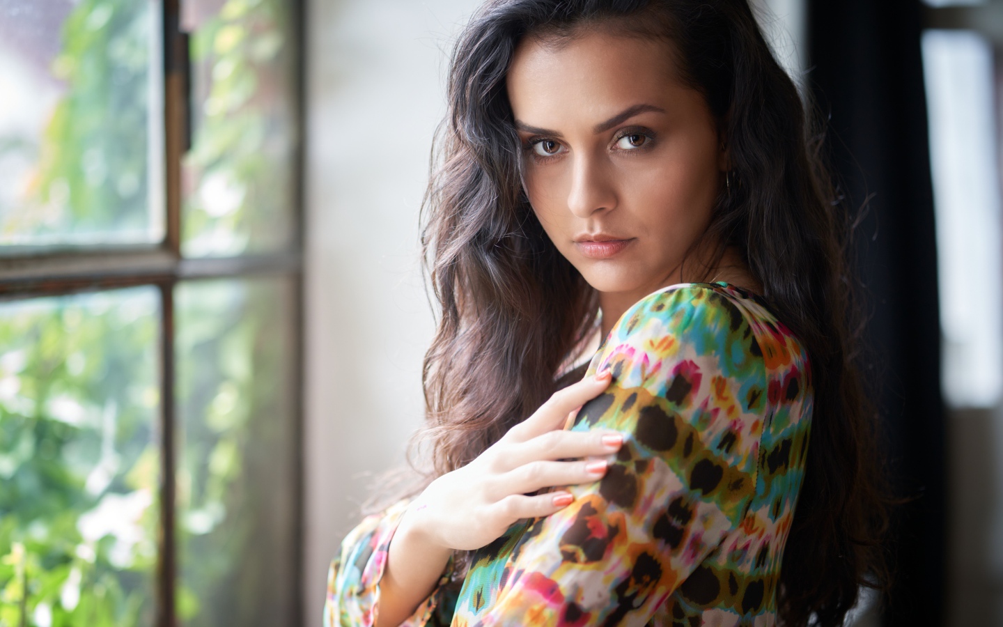 Длинноволосая кареглазая девушка стоит у окна