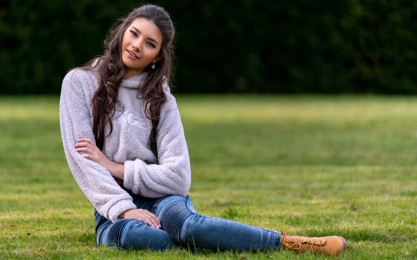 Молодая длинноволосая девушка сидит на траве 