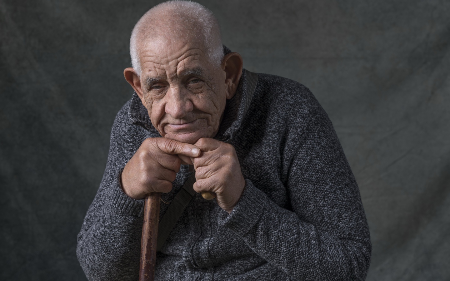 Пожилой мужчина в теплом свитере на сером фоне 