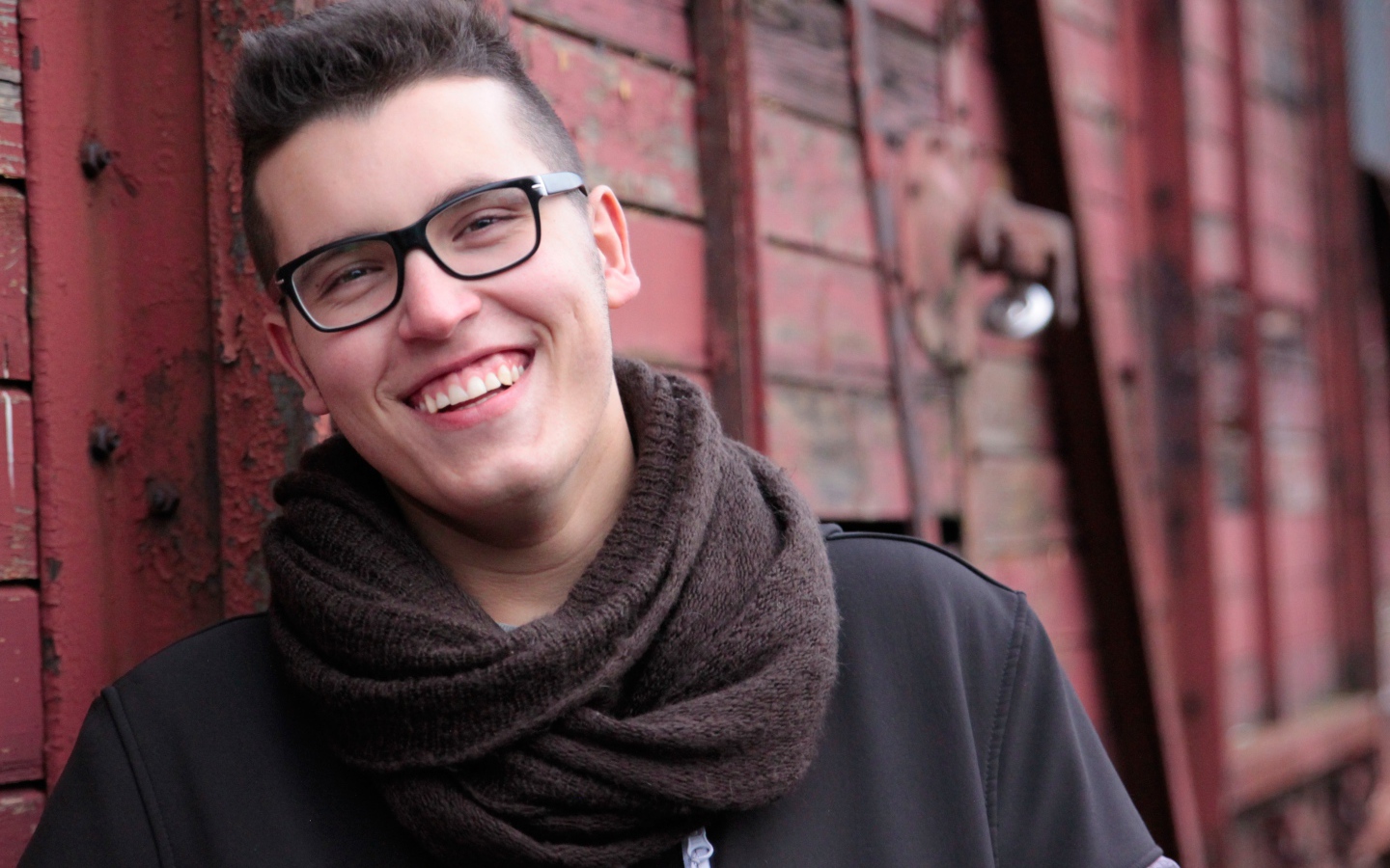 Улыбающийся мужчина в очках у стены 