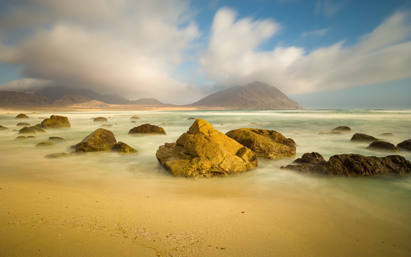 Большие камни лежат в воде на песке 